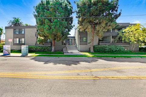 A street view of a residential area with two houses, trees, and a clear sky.