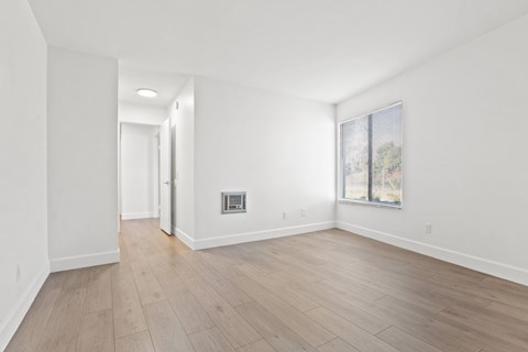 A room with wooden flooring and a window showing trees outside.
