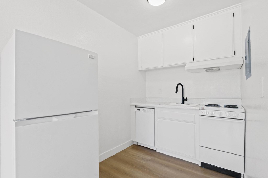 A white kitchen with a refrigerator, sink, and stove.