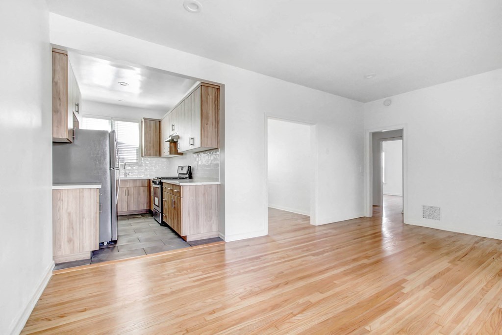 the living room and kitchen of a house with wood floors and white walls
