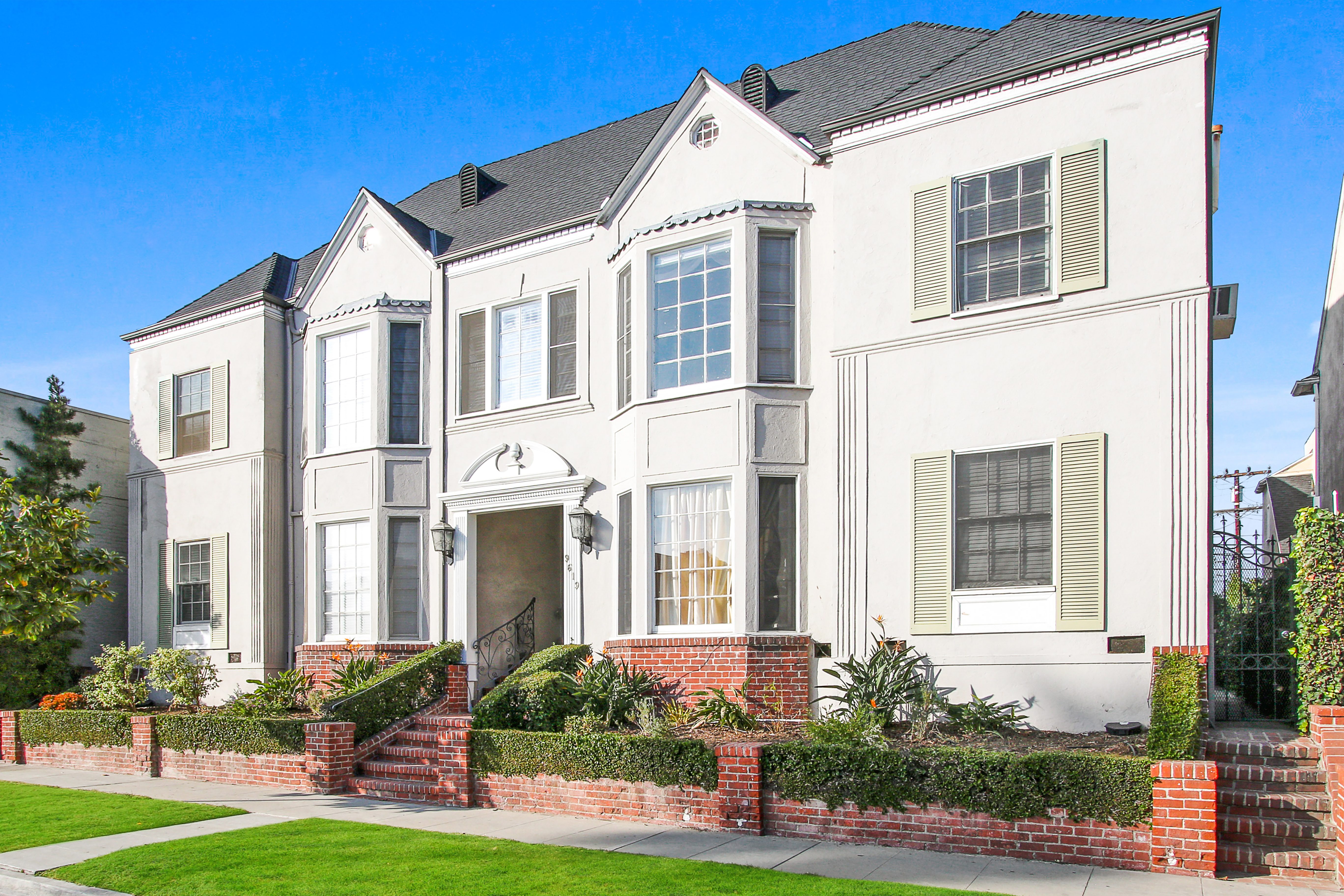 A white two-story house with a red brick wall in front.