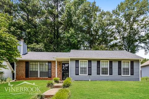 a small gray house with black shutters and a lawn