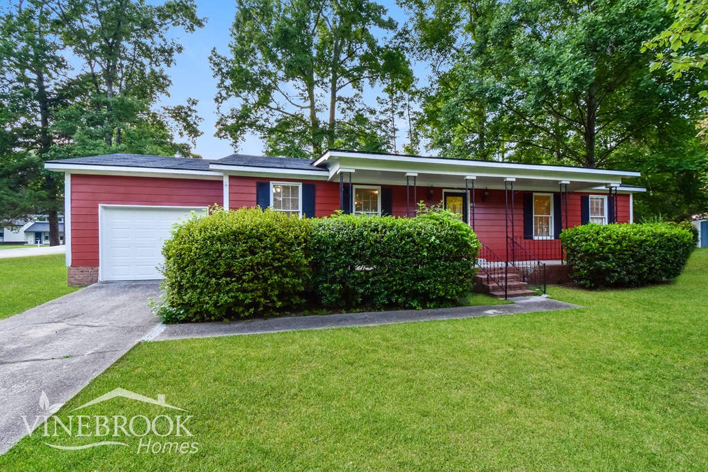 a red house with a lawn and bushes in front of it