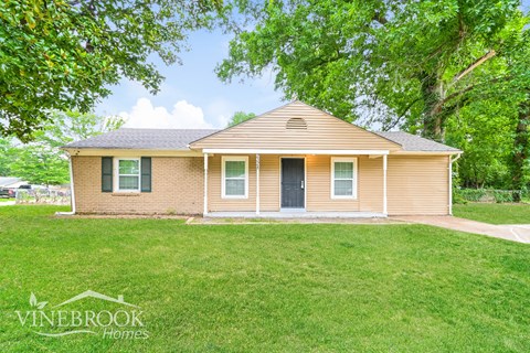 a small brown house with a lawn and trees