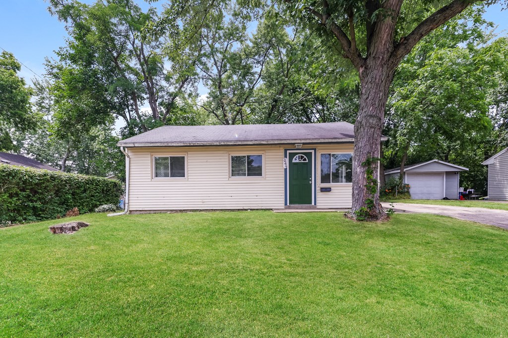 a small yellow house with a green door and a tree