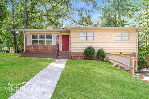 a small yellow house with a red door and a lawn