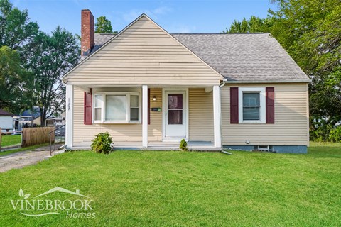 a small tan house with red shutters and a lawn