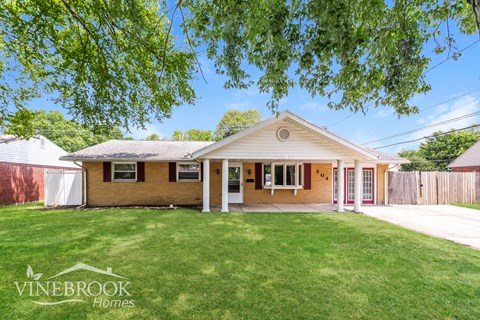 a small brick house with a grassy yard and a white porch