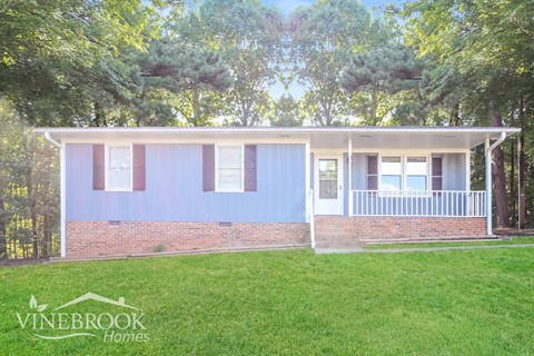 a small blue house with a lawn and trees