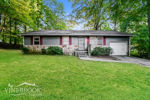 a small gray house with red shutters and a lawn