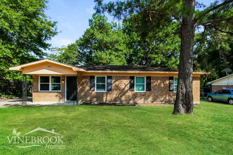 a small brick house with a lawn and trees