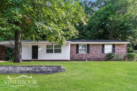 a small brick house with a lawn and trees