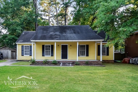a yellow house with a black roof and a yard