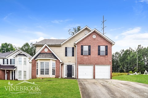 a brick house with white garage doors and a lawn