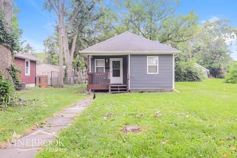 a small gray house in a yard with grass and trees