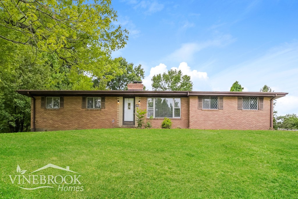 A house with a green lawn and trees in the background is for sale.