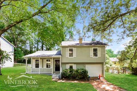 a small yellow house with a porch and a tree