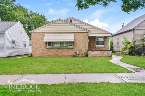 a small brick house with a yard and a sidewalk