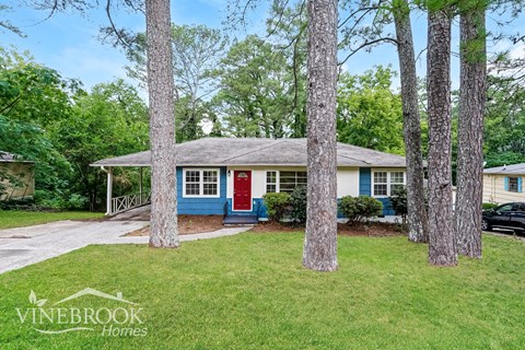 a blue and white house with a red door and trees