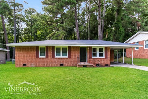 a small brick house with a green lawn and some trees
