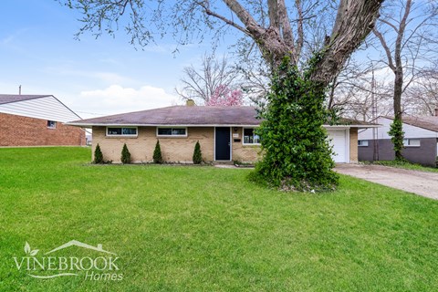 A house with a green lawn and a tree in front of it.