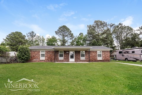 A house with a lawn in front of it and trees in the background.