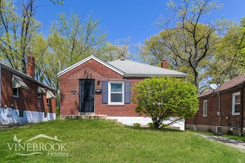 A brick house with a black door and a tree in front of it.