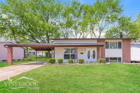 A house with a covered patio and a well-kept lawn.