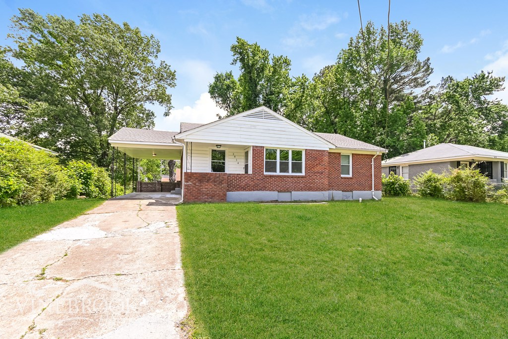 A house with a brick facade and a white roof is surrounded by a grassy lawn and trees.