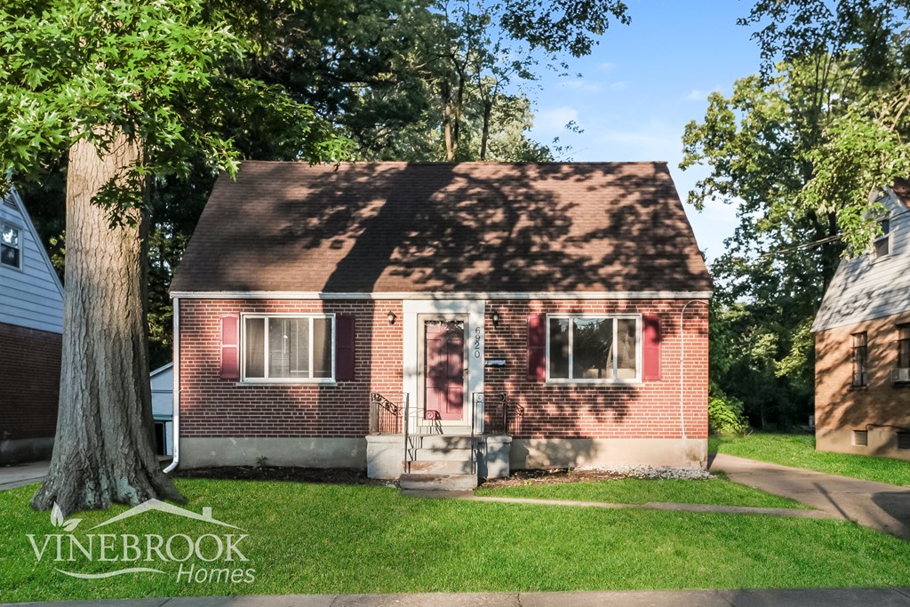 A small red brick house with a tree in front of it.