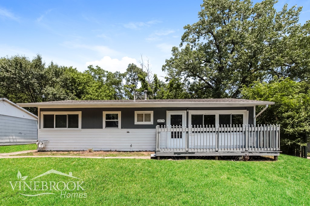 A house with a porch and a fence is surrounded by greenery.