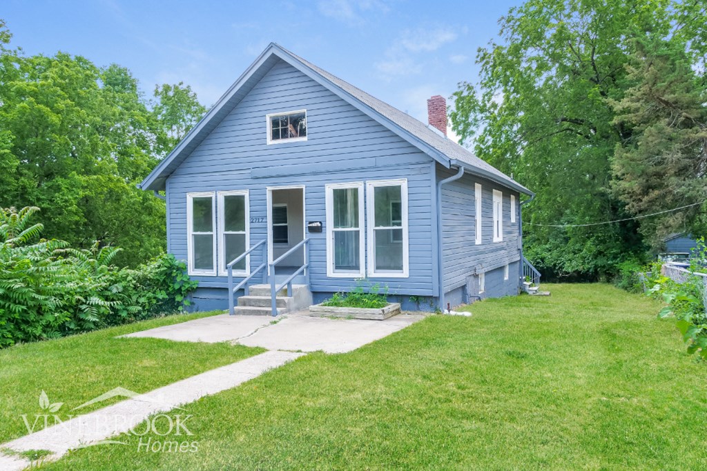 a blue house with white trim and a lawn and trees