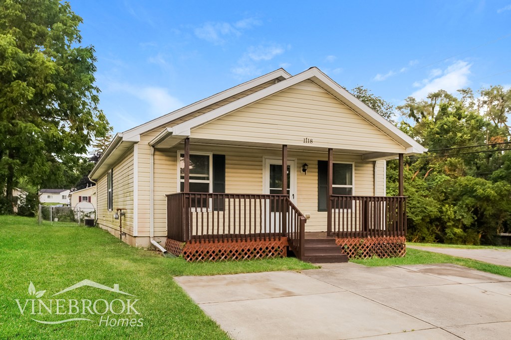 the front of a yellow house with a porch and a sidewalk
