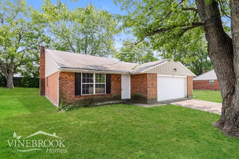 the front of a brick house with a yard and a tree