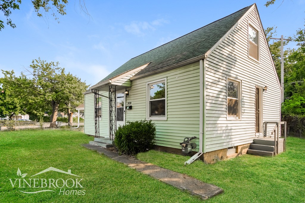 a small green and white house with a lawn and trees