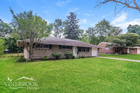 a small brown house with a grass lawn and trees