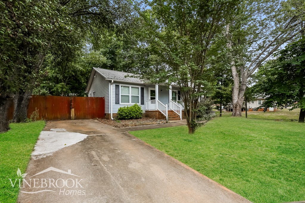 a small blue house with a yard and trees and a driveway