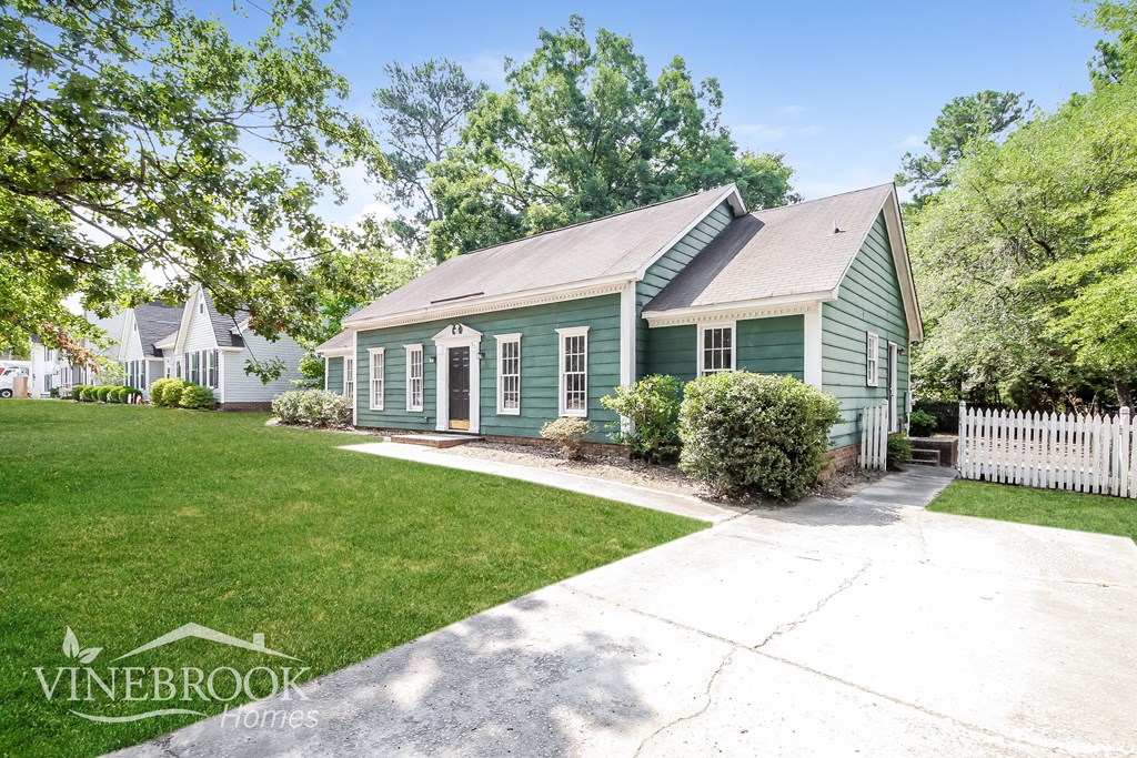 a green house with a white picket fence and a lawn