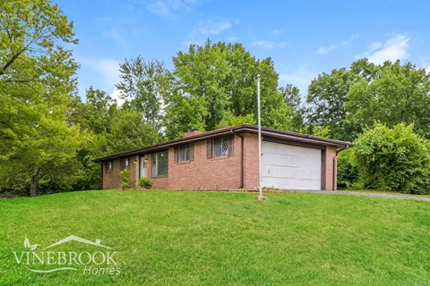 A house with a garage is surrounded by greenery and has a sign that says Vinebrook Homes.