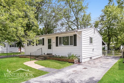 a small white house with a driveway and trees