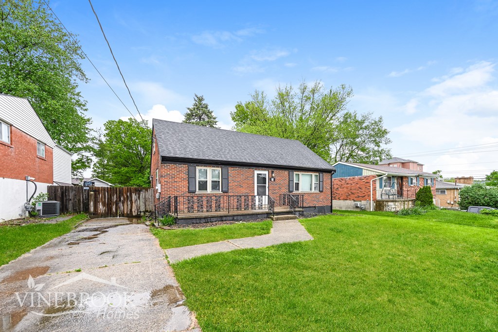 A house with a brick exterior and a black roof is surrounded by a grassy area and other residential buildings.