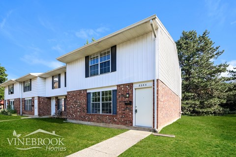 A white house with a brick wall and a sign that says Vinebrook Homes.
