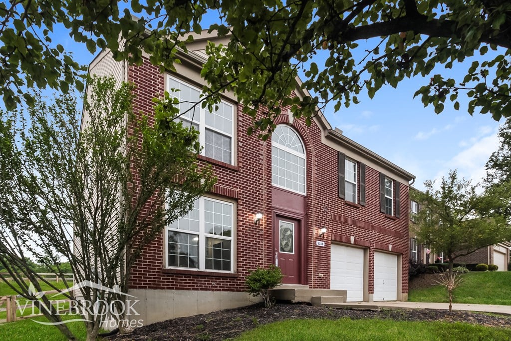 A red brick house with a white garage door and a tree in front.