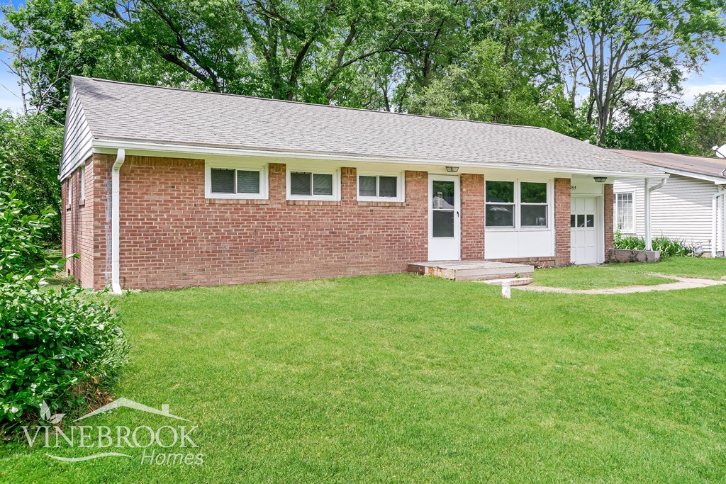 A house with a white door and windows is surrounded by a green lawn.