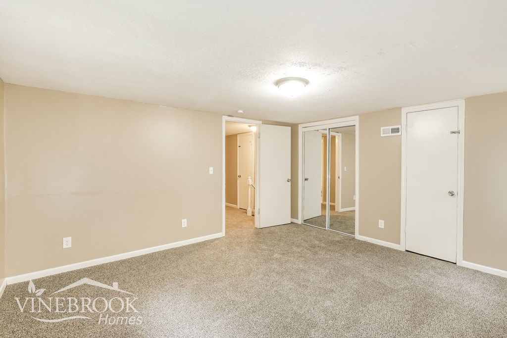 a living room with a carpeted floor and a mirrored closet