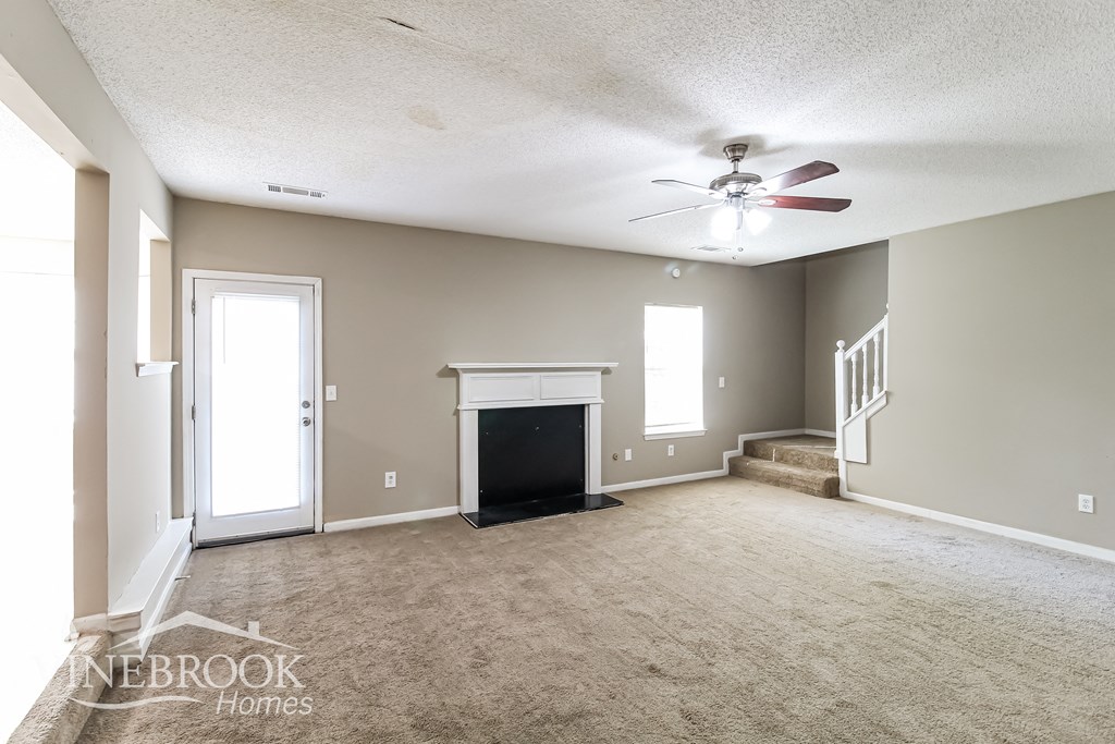 an empty living room with a fireplace and a ceiling fan