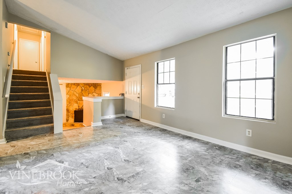 an empty living room with a staircase and a door to a kitchen