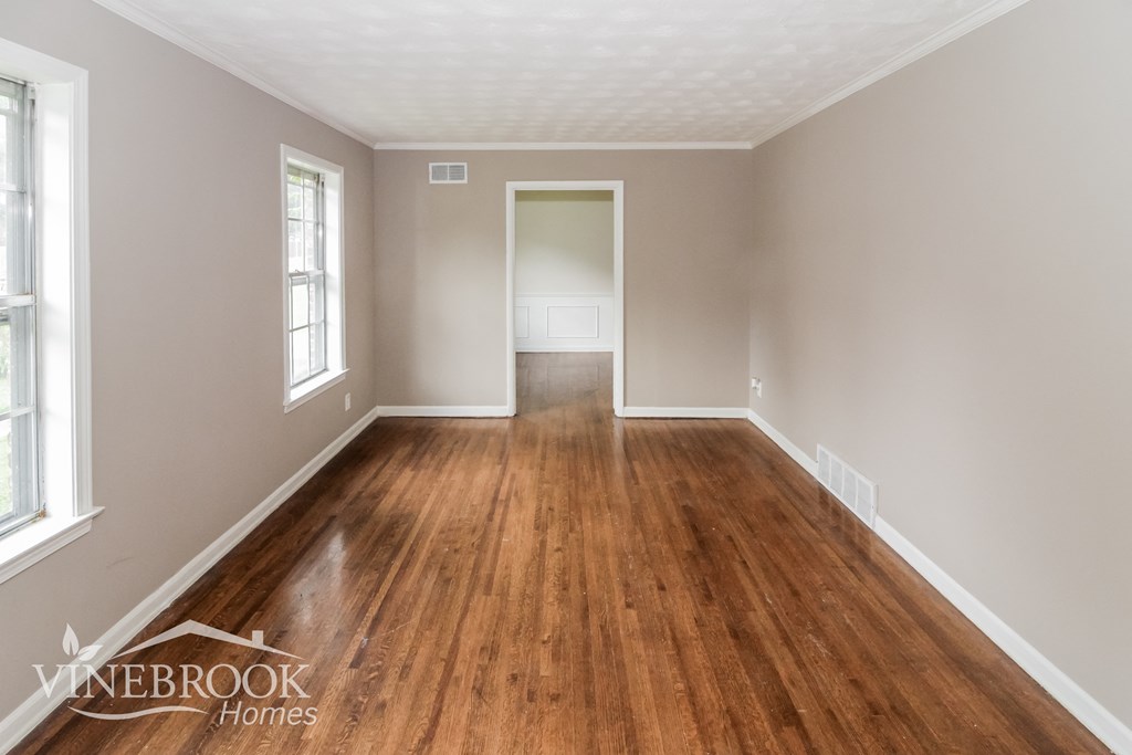 A room with wooden floors and white walls, with a doorway leading to another room.