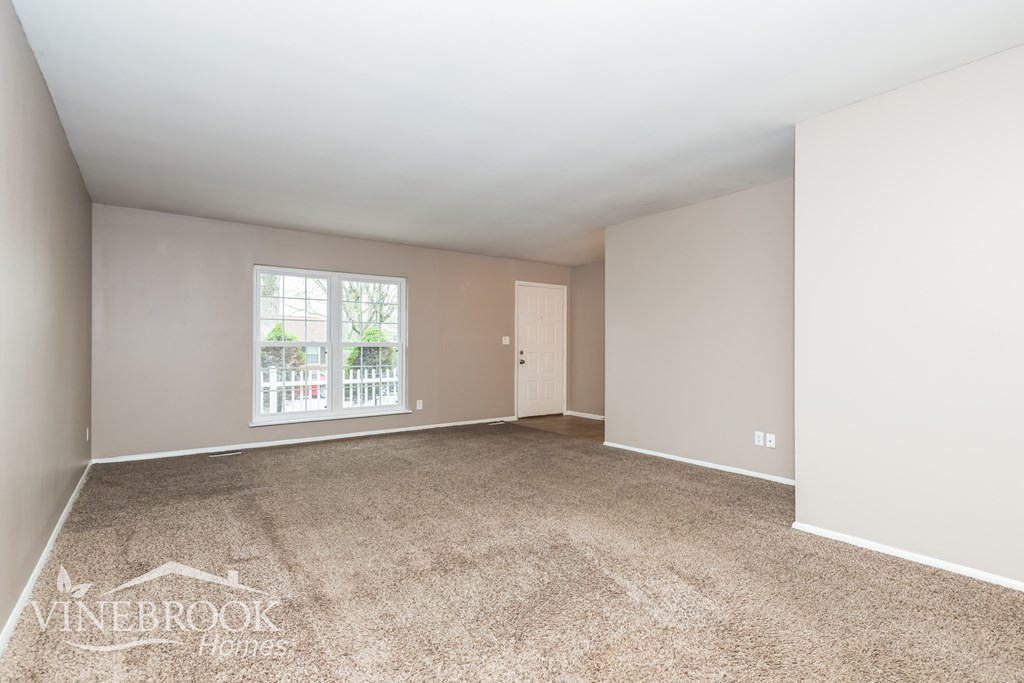 A room with a carpeted floor and a window showing a balcony with a railing.
