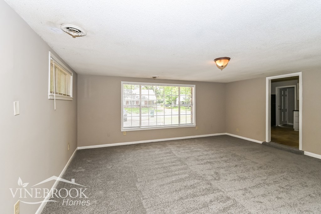 A room with a carpeted floor and a window with blinds.